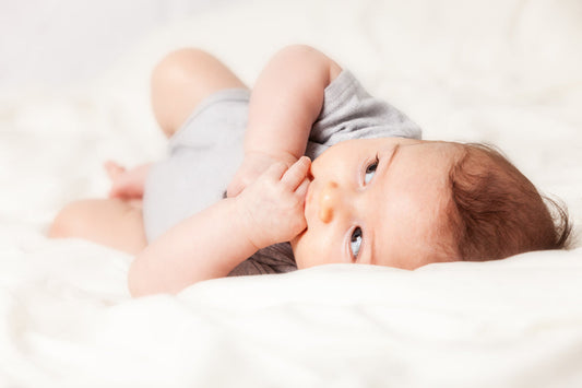 Baby lying on the bed with hands in mouth and eyes open