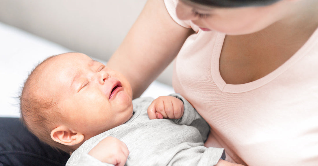 A woman is holding a crying baby with a pained expression on her arm.