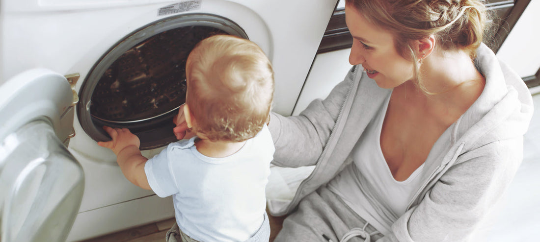 Mother and toddler stand together in front of the open washing machine