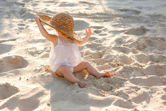 Baby in a dress on the beach with a sun hat.