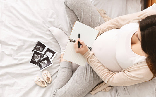 Pregnant woman looks at ultrasound images and writes baby names in a notebook.