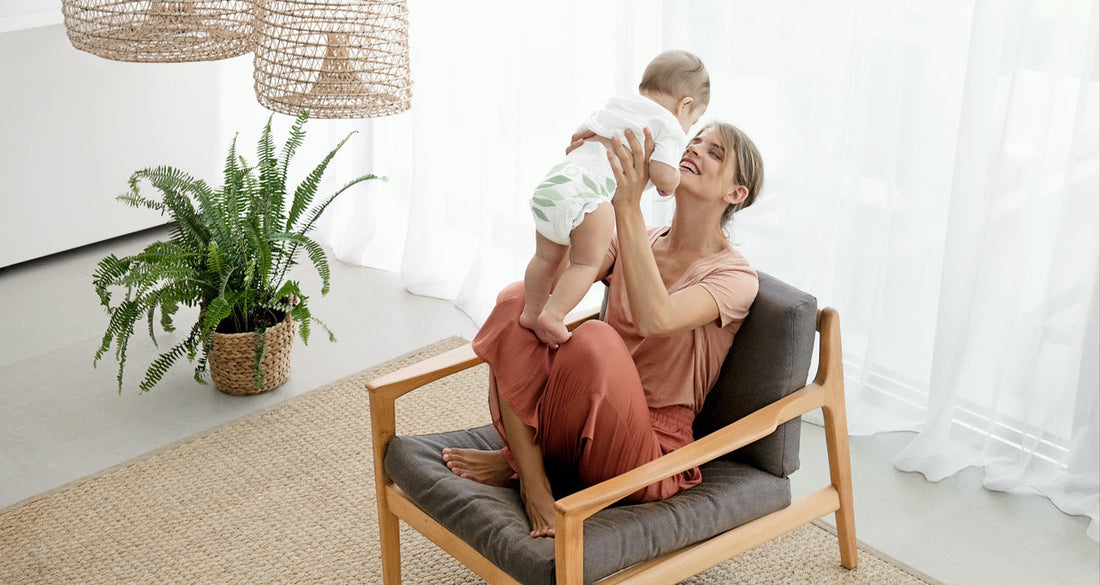 Mother is playing with her baby on her lap, in the background the changing table can be seen.