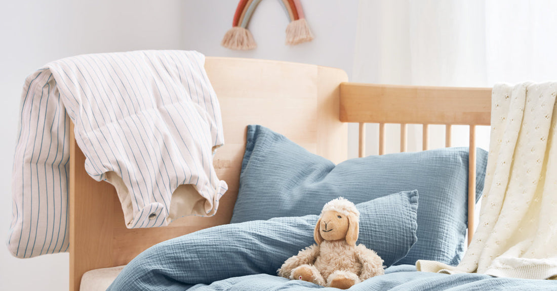 Muslin bedding, a sleeping bag, and a stuffed animal are on a child's bed.