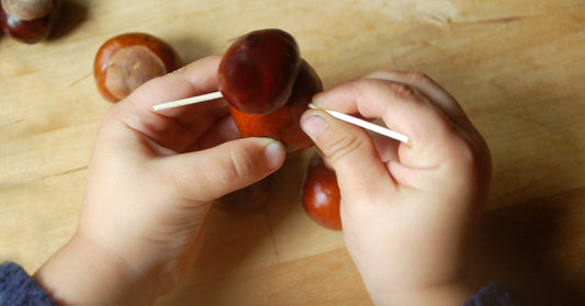 Children's hands craft a chestnut figure with toothpicks