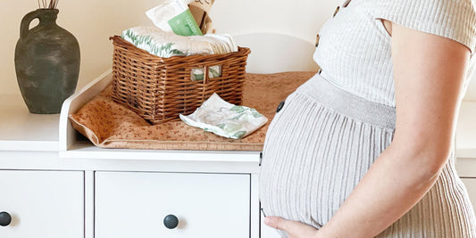 Pregnant woman caresses baby bump in front of changing table with LILLYDOO green diapers