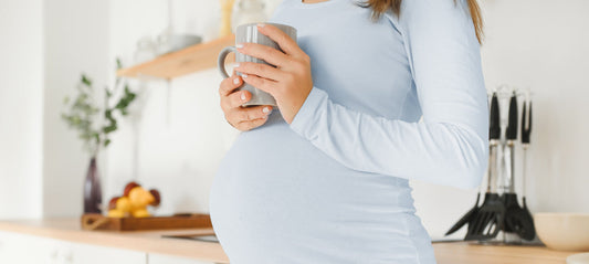Pregnant woman holding a cup of raspberry leaf tea in her hand.