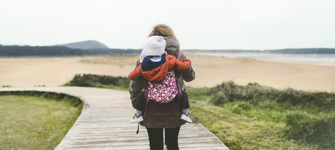 Mother carries her baby in the carrier on her back.