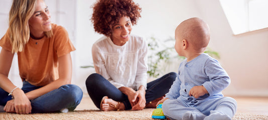 Two mothers are sitting on the floor with their baby and playing