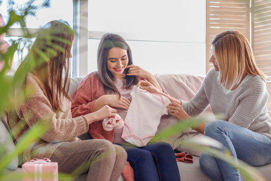 A pregnant woman is sitting with two friends. She has just received baby clothes as a gift.