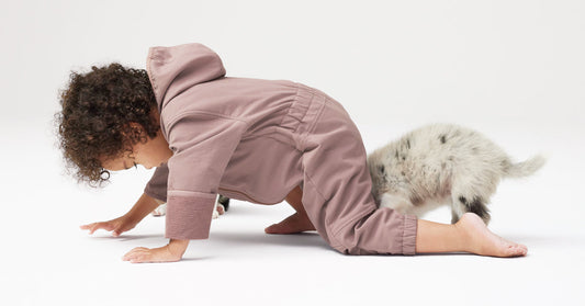 Toddler in cozy children's clothing crawls along the floor with a pet.