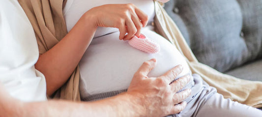Pregnant couple sitting together on the sofa, he is stroking her belly.