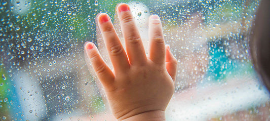 Child looking out the window at the falling rain