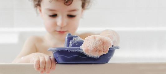 little boy sitting in the bathtub playing with his bath toys