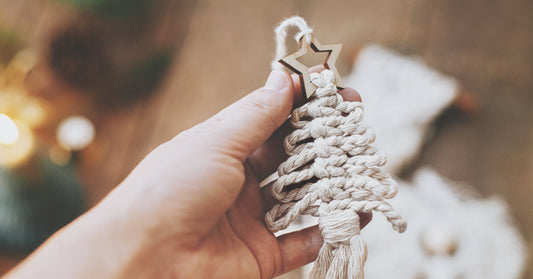 Woman holding a macramé-knotted tree decoration in the shape of a Christmas tree with a star.