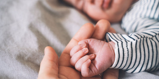 The hand of an adult holds a small baby hand while the baby is sleeping.