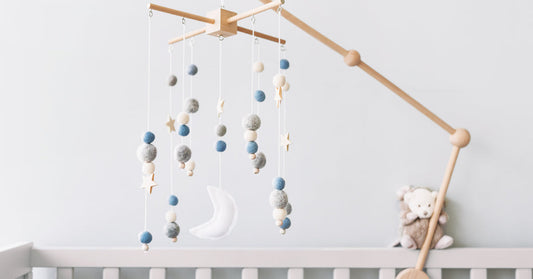 A mobile made of stars and a moon hangs above a wooden children's bed, on which a stuffed animal is standing.