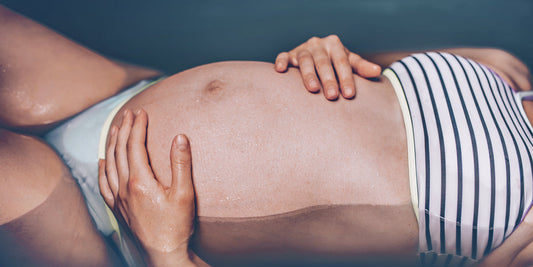 Pregnant woman in a bikini is lying in the water.